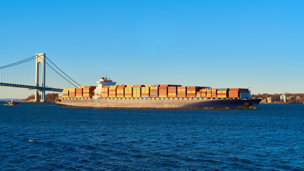 A fully loaded freighter on deep blue water near a suspension bridge.